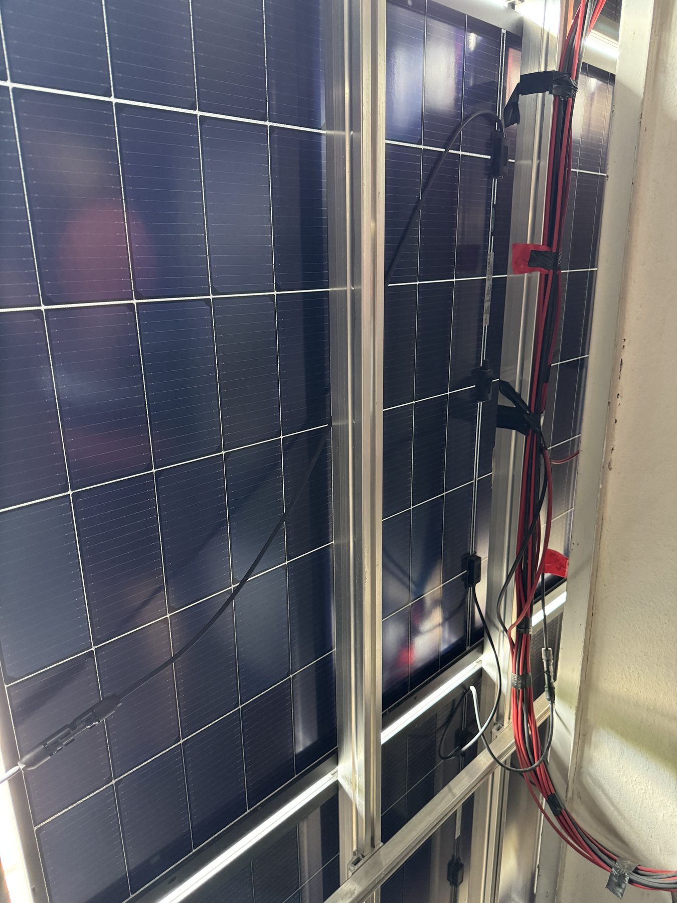 Photovoltaikmodule von innen im Fassadenzwischenraum, dazwischen die Aluminium-Unterkonstruktion und der rot-schwarze DC-Strang an der Wand