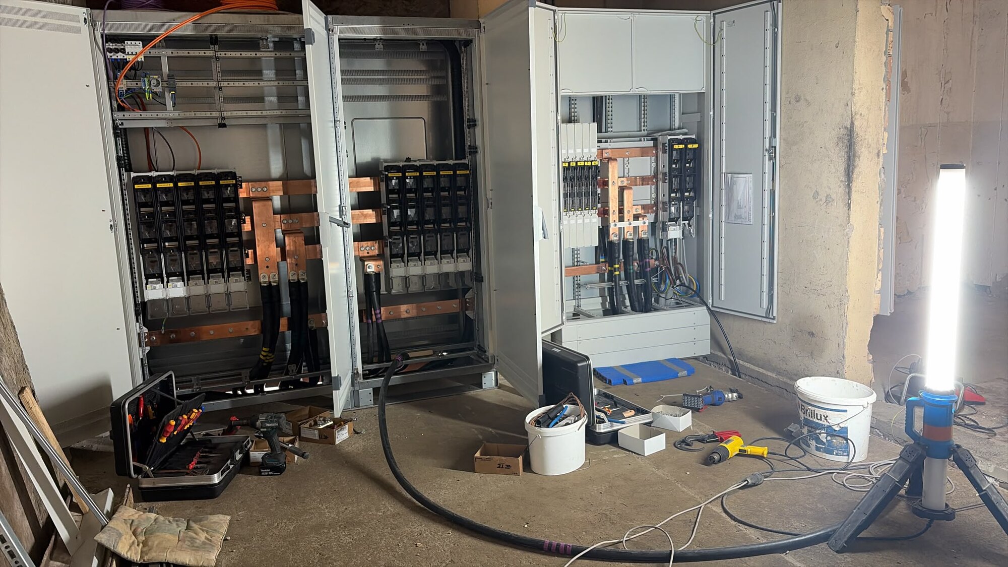 Zwei Niederspannungshauptverteilungen stehen offen im Rohbau, Schienen und Sicherungslasttrennschalter gesetzt, Kabel eingezogen, Werkzeug und Baustrahler am Boden